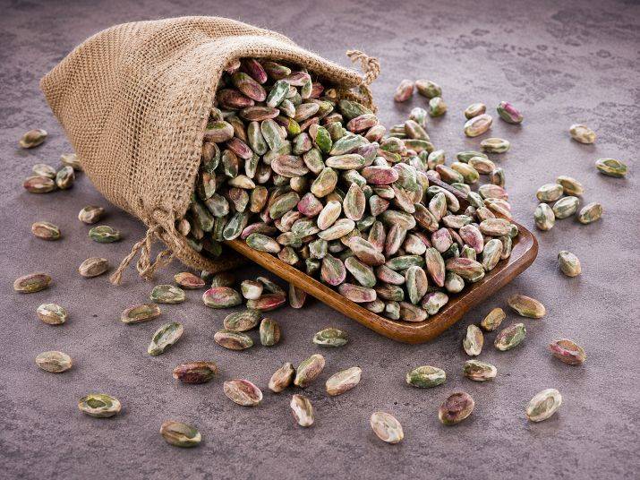 Shelled pistachios spilling from a burlap sack onto a wooden tray.