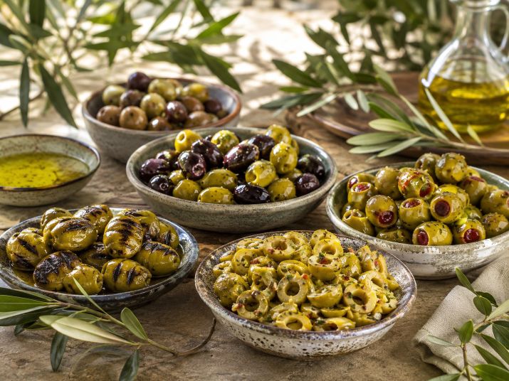 An assortment of marinated, sliced, stuffed, and grilled olives in ceramic bowls.