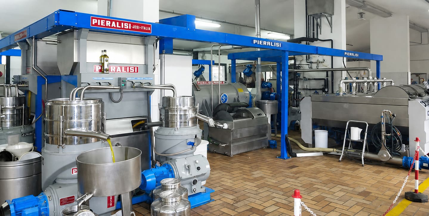 Azeite de oliva extra virgem recém-extraído jorrando de máquinas de centrifugação de aço inoxidável da marca Pieralisi para um recipiente de coleta de metal dentro de um lagar industrial.