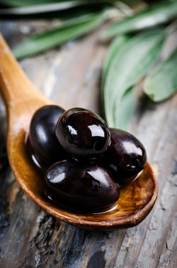 Premium black olives prepared for high-quality olive oil export served on a traditional wooden spoon.